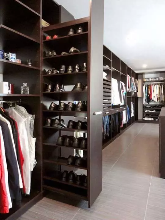 Vestidor a medida con estanterías de madera oscura y zapateras integradas, ropa organizada en perchas y estantes